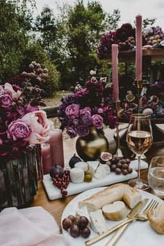 a table topped with plates and glasses filled with food next to candles, flowers and vases