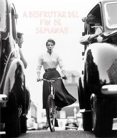 black and white photograph of woman on bicycle in front of parked cars with other vehicles