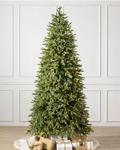 a christmas tree with presents under it on a wooden floor in front of a white wall