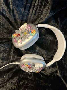 two white headphones sitting on top of a black cloth covered bed with floral decorations