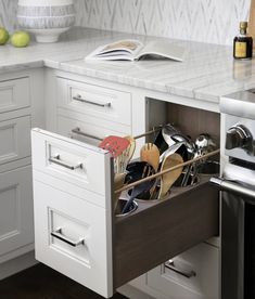 an open drawer in the middle of a kitchen with utensils and spoons