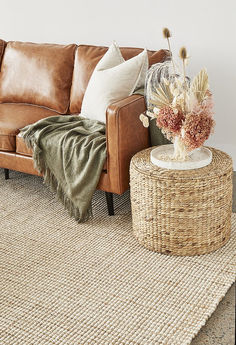 a brown leather couch sitting on top of a rug next to a table with flowers