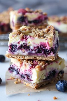 three blueberry cheesecake bars stacked on top of each other next to fresh blueberries