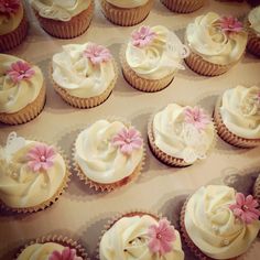 there are many cupcakes with white frosting and pink flowers on them in the box