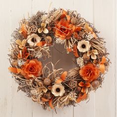 a wreath with orange flowers and dry grass on a white wooden background, top view