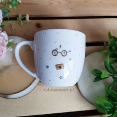 a coffee cup with a face drawn on it next to some pink flowers and greenery