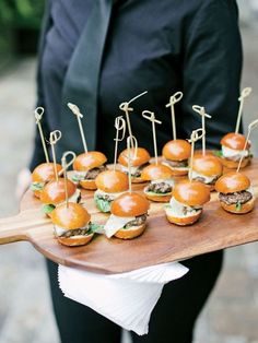 a person holding a tray with mini burgers on it and toothpicks in the middle