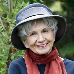 an older woman wearing a hat and scarf in front of some trees with green leaves