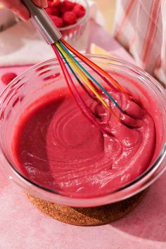 someone mixing raspberry sauce in a glass bowl