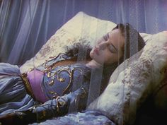 a woman laying on top of a bed next to a window covered in sheer curtains