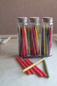 three glass jars filled with different colored candles next to two yellow and one red sticks