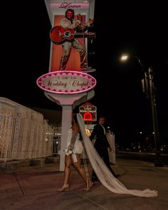 a bride and groom walk past a lighted sign