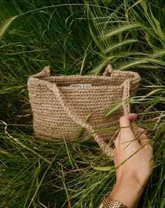 a hand holding a crocheted bag in the grass with it's handle