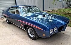 a blue muscle car parked in front of a garage