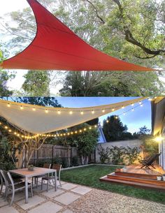 an outdoor dining area with patio furniture and string lights strung over the table, along with a red shade sail