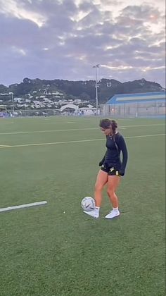 a female soccer player on the field with a ball in her hand and buildings in the background