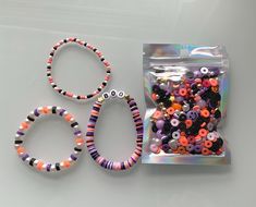 three bracelets and two bag of beads sitting on a table next to each other