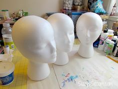 three white mannequin heads sitting on top of a table next to paint bottles