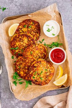 crab cakes with lemon wedges and ketchup on a tray next to some dipping sauce