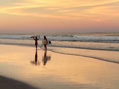 two people walking on the beach with their surfboards