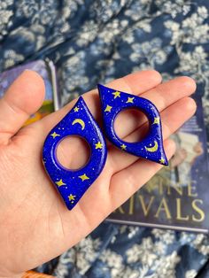 a pair of blue earrings with stars and moon shapes on them, held in someone's hand