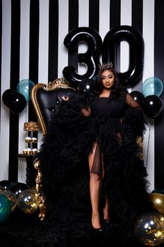 a woman in a black dress sitting on a chair with balloons and streamers around her