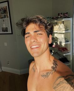 a man with tattoos on his chest smiling at the camera while standing in front of a closet