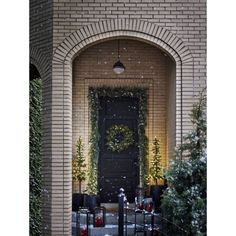 a black front door surrounded by greenery and christmas decorations with snow falling on the ground