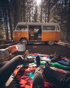 two people sitting on a blanket in front of a van with their feet propped up