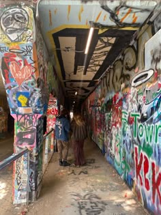 two people are walking down an alley with graffiti on the walls and underpasss