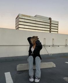 a woman is sitting on a bench talking on her cell phone in the parking lot