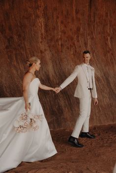 a bride and groom holding hands in front of a wall