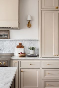 a kitchen with white cabinets and marble counter tops, gold pulls on the cupboards