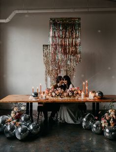 two people sitting at a table surrounded by balloons and candles in front of the couple