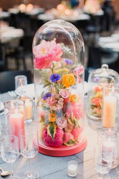 an arrangement of flowers under a clochet on a table with candles and glasses