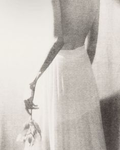 a black and white photo of a woman in a long dress holding a flower bouquet