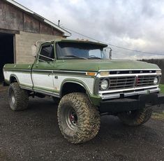 a large green truck parked in front of a barn