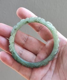 This Jadeite bangle outer is rounded and and flatten on the inside by hand. This jade bangle untreated Type-A jadeite jade. It has been polished on the inside and outside. The photos have not been altered or changed at all. *Bangle Shape: Flat Inner, Hand Carved Floral Design Round Outer *Color: Icy Cloudy Imperial Green, Apple Green (Moss-In-Snow) *Luster: Vitreous *Transparency: Translucent *Inside Width: 58.3mm *Bangle Width: 14.8 mm *Weight: 60 Grams *Size: Medium *Texture: Fine and Smooth * Spiritual Carved Round Bracelets, Spiritual Round Carved Bracelets, Carved Jade Round Bracelets, Carved Jade Bracelets, Green Carved Round Bangle, Carved Round Bracelets For Wedding, Carved Round Wedding Bracelets, Wedding Carved Round Bracelets, Carved Jade Bracelet