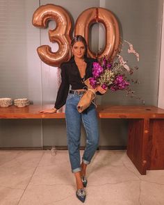 a woman standing in front of a table with flowers and balloons that say 30 on it