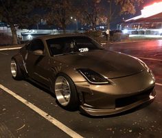 a silver sports car parked in a parking lot at night with its hood up and lights on