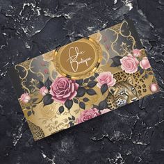 a black and gold business card with pink roses on it, sitting on a marble surface