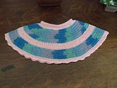 a crocheted blue and pink sweater sitting on top of a wooden table next to a potted plant