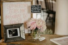 pink flowers are in a vase next to a framed photo and a sign that says, something jesus loves me is coming to town