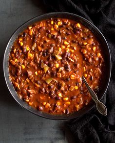 a bowl filled with chili and corn on top of a black cloth next to a spoon