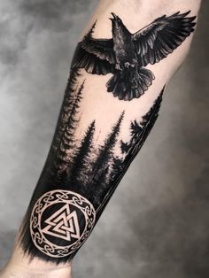 an arm with a bird flying over trees and a triangle tattoo on the left forearm