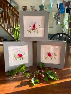 three framed pictures with red birds on them sitting on a table next to some leaves