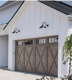 a white house with two garage doors and three lights on each side of the door