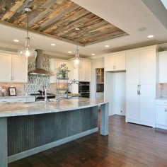 a large kitchen with an island in the middle and wood floors on both sides, along with white cabinets