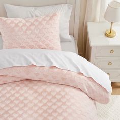 a bed with pink and white comforters in a bedroom next to a lamp on a nightstand