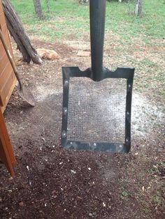 a metal shovel sitting on top of a dirt ground next to a wooden fence and trees